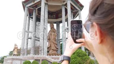 女用智能手机拍摄观音观音或佛寺观音雕像。 访问精神